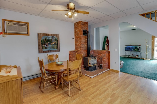 dining room with ceiling fan, a wood stove, light hardwood / wood-style flooring, and a paneled ceiling