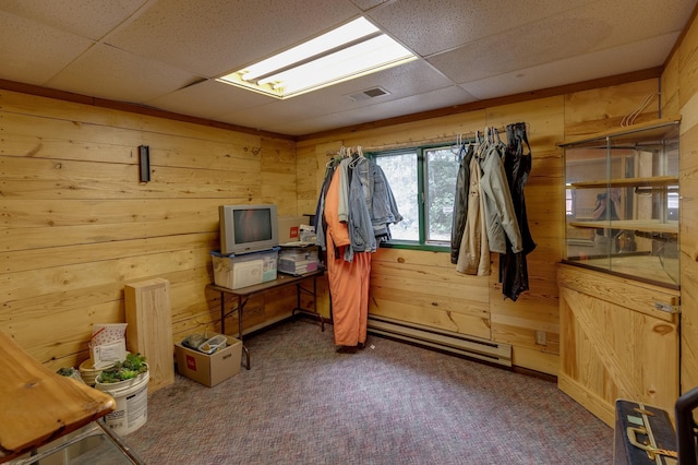 interior space featuring a paneled ceiling, wooden walls, baseboard heating, and carpet