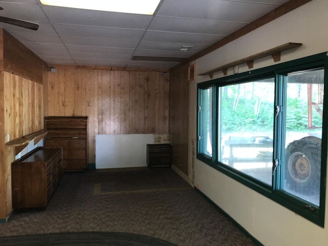 interior space featuring wooden walls, dark colored carpet, and a drop ceiling