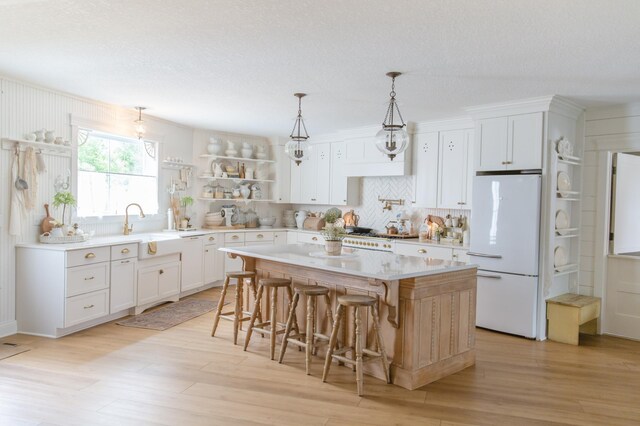 kitchen featuring white refrigerator, light hardwood / wood-style flooring, a center island, white cabinetry, and a breakfast bar area