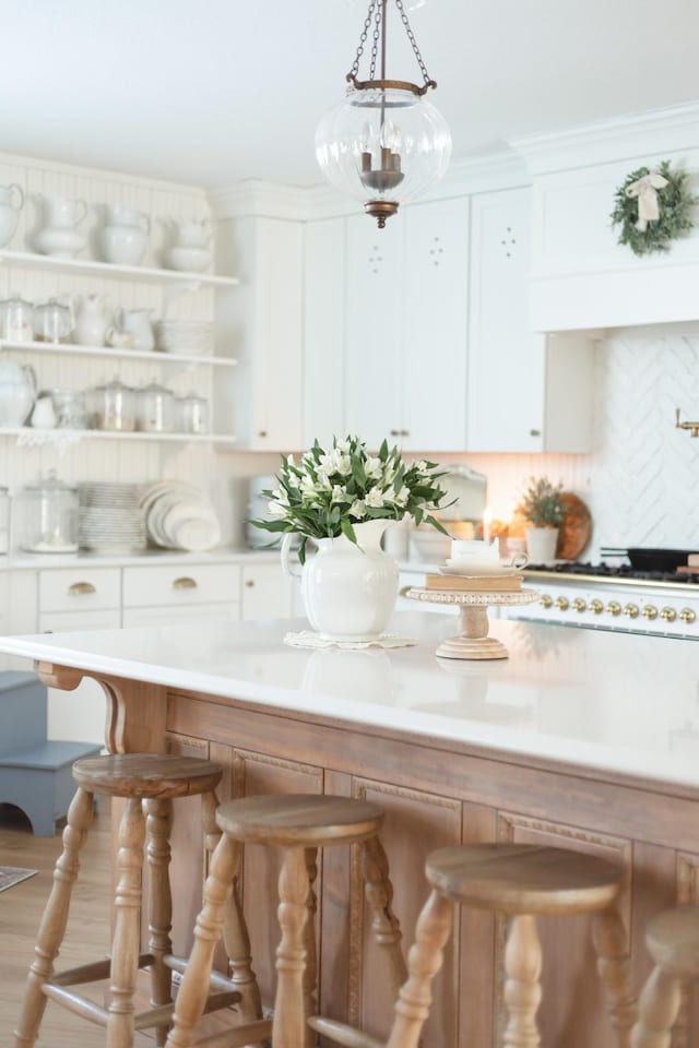 kitchen featuring pendant lighting, hardwood / wood-style flooring, a breakfast bar area, white cabinetry, and cooktop