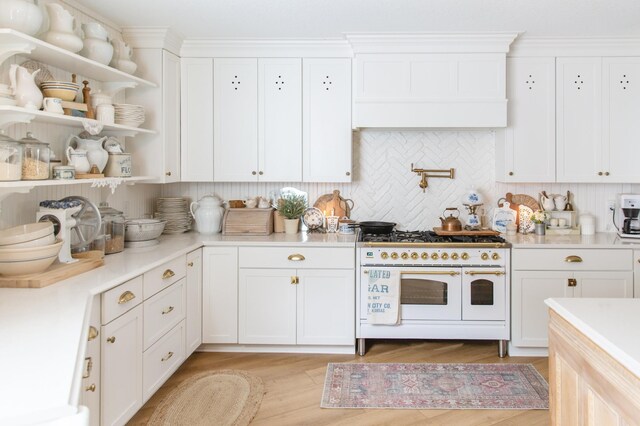 kitchen with backsplash, white cabinets, light hardwood / wood-style floors, and range with two ovens