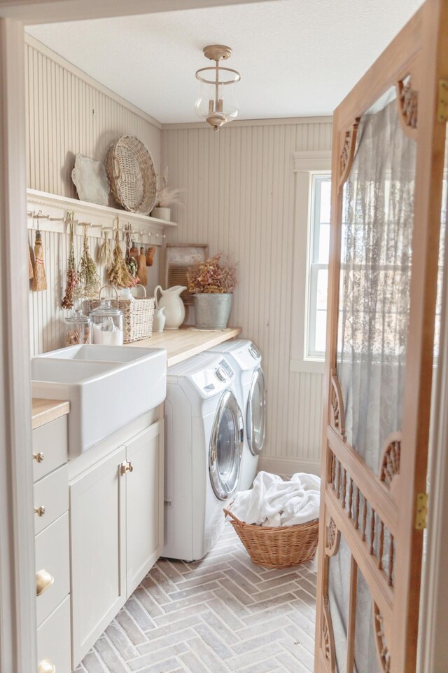 washroom featuring wood walls, cabinets, crown molding, sink, and washing machine and dryer