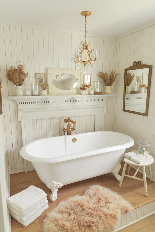 bathroom featuring wood walls, wood-type flooring, a tub to relax in, and an inviting chandelier