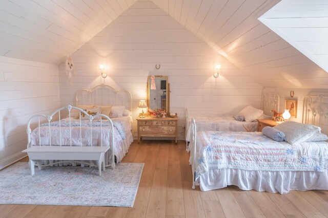 bedroom with wooden walls, light hardwood / wood-style floors, and lofted ceiling