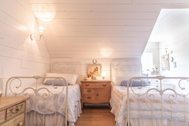 bedroom featuring wood walls, lofted ceiling, and light hardwood / wood-style flooring