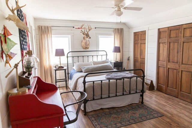 bedroom with ceiling fan, multiple closets, wood-type flooring, and vaulted ceiling