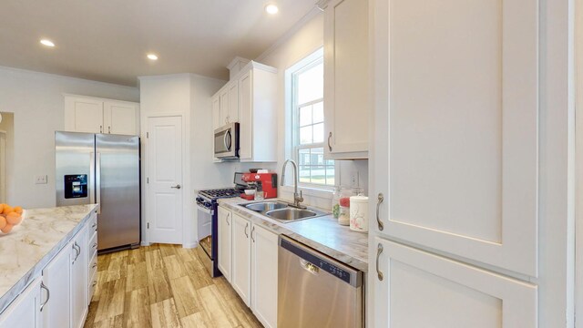 kitchen with appliances with stainless steel finishes, light stone counters, light hardwood / wood-style floors, sink, and white cabinetry