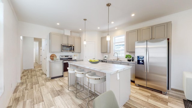 kitchen featuring stainless steel appliances, hanging light fixtures, ornamental molding, a kitchen island, and light wood-type flooring