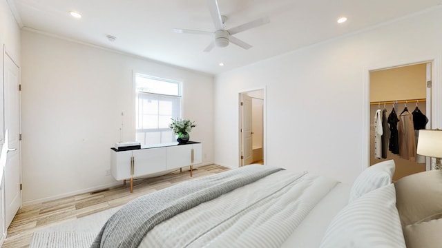 bedroom featuring a walk in closet, ornamental molding, ensuite bath, light hardwood / wood-style floors, and ceiling fan