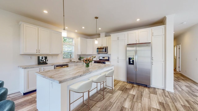 kitchen with a kitchen island, white cabinetry, appliances with stainless steel finishes, decorative light fixtures, and light hardwood / wood-style floors