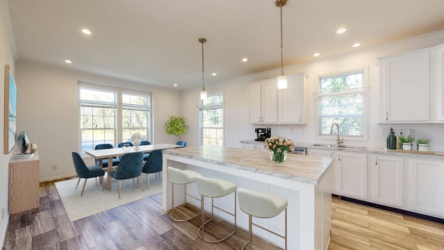 kitchen featuring white cabinetry, sink, hanging light fixtures, a kitchen island, and light wood-type flooring