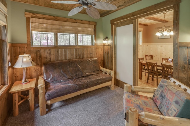 sitting room with wood walls, carpet floors, wooden ceiling, and ceiling fan with notable chandelier