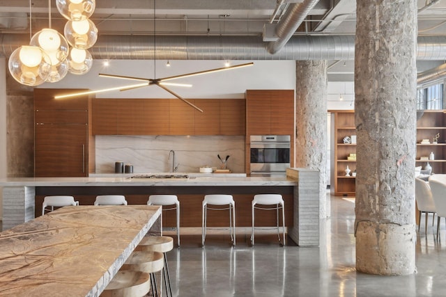 kitchen with backsplash, appliances with stainless steel finishes, decorative light fixtures, a kitchen bar, and a chandelier