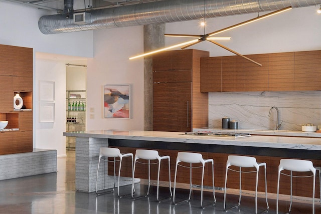 kitchen with sink, a high ceiling, stainless steel gas cooktop, a kitchen breakfast bar, and decorative backsplash