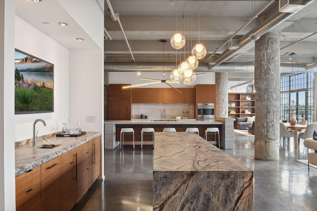 kitchen featuring decorative light fixtures, stainless steel oven, light stone counters, and sink