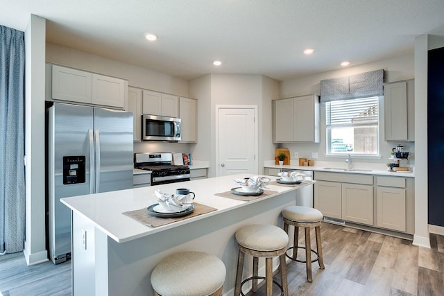 kitchen with sink, a kitchen breakfast bar, light hardwood / wood-style floors, a kitchen island, and appliances with stainless steel finishes