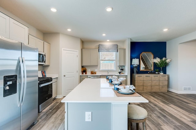 kitchen with a breakfast bar, appliances with stainless steel finishes, a center island, and light hardwood / wood-style floors