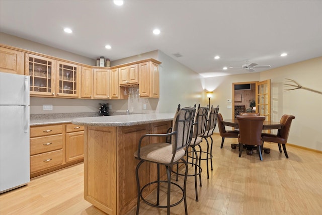 kitchen with a kitchen breakfast bar, white fridge, ceiling fan, light brown cabinetry, and light wood-type flooring