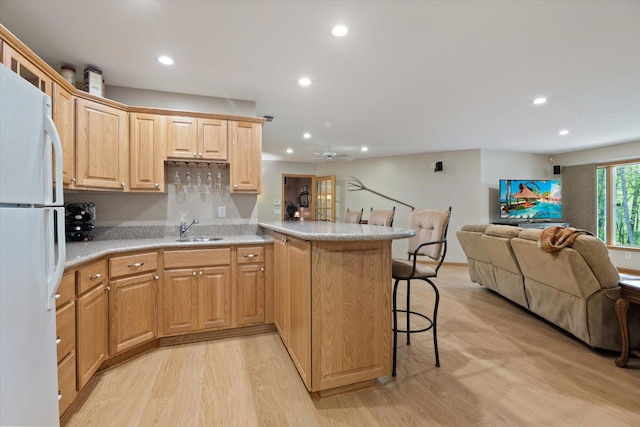 kitchen featuring ceiling fan, sink, white fridge, a kitchen breakfast bar, and light wood-type flooring