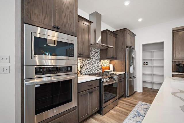 kitchen featuring light stone counters, appliances with stainless steel finishes, light hardwood / wood-style flooring, wall chimney range hood, and tasteful backsplash