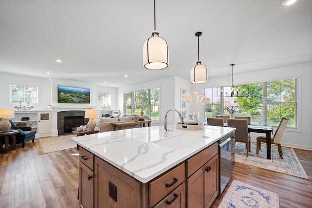 kitchen featuring hanging light fixtures, light wood-type flooring, an island with sink, a notable chandelier, and sink