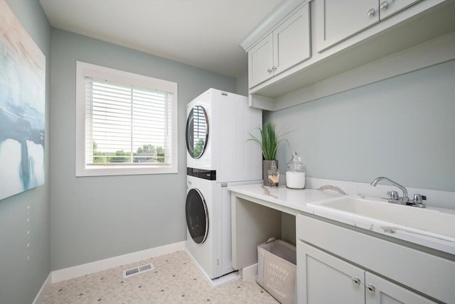 clothes washing area featuring sink, cabinets, light tile floors, and stacked washing maching and dryer