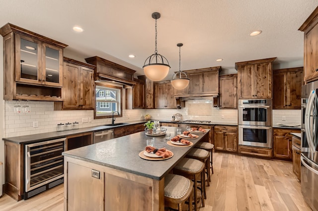 kitchen featuring a center island, stainless steel appliances, beverage cooler, decorative light fixtures, and light wood-type flooring