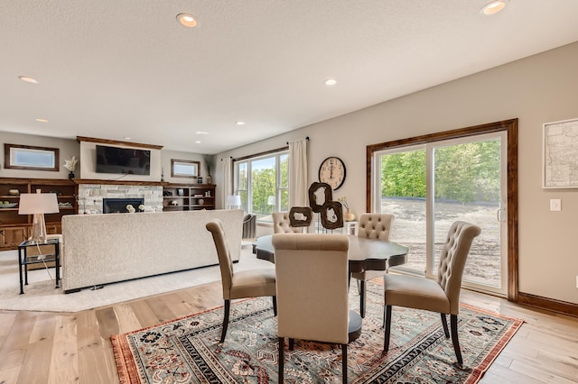 dining room featuring a fireplace, light wood-type flooring, and a textured ceiling