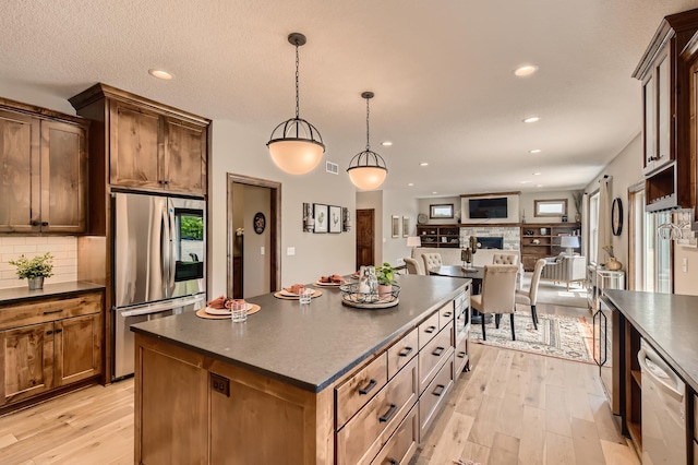 kitchen featuring a center island, light hardwood / wood-style floors, appliances with stainless steel finishes, tasteful backsplash, and decorative light fixtures