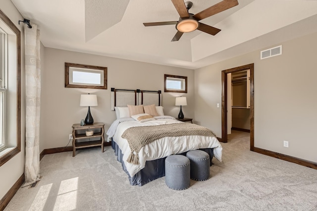 bedroom featuring ceiling fan, multiple windows, and a tray ceiling