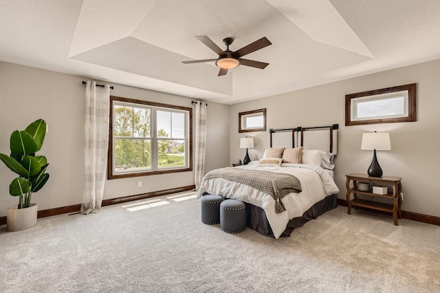 bedroom with ceiling fan, light colored carpet, and a tray ceiling