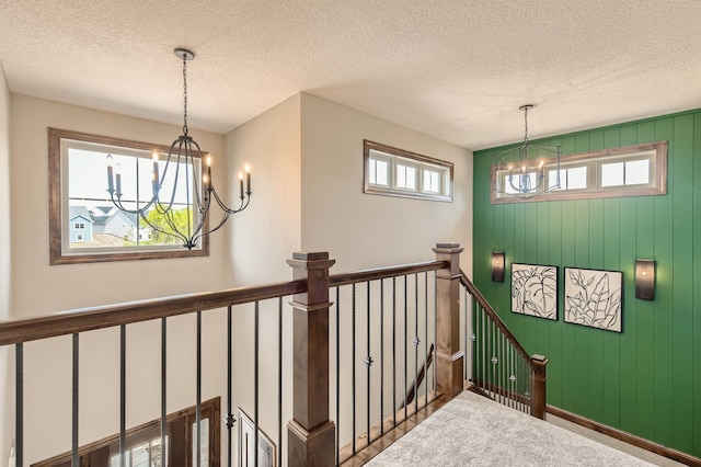 staircase with carpet floors, a healthy amount of sunlight, an inviting chandelier, and a textured ceiling