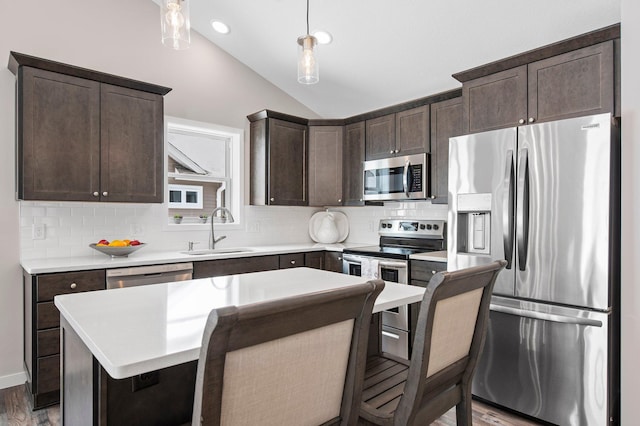 kitchen featuring a kitchen island, stainless steel appliances, sink, hanging light fixtures, and vaulted ceiling