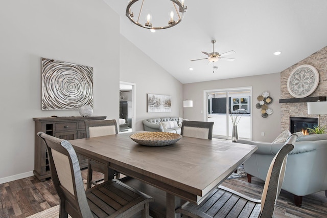 dining area with high vaulted ceiling, dark hardwood / wood-style flooring, ceiling fan with notable chandelier, and a stone fireplace