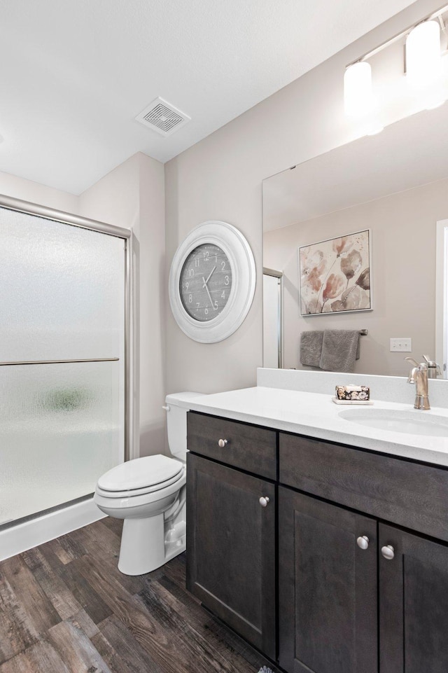 bathroom with hardwood / wood-style flooring, a shower with shower door, vanity, and toilet