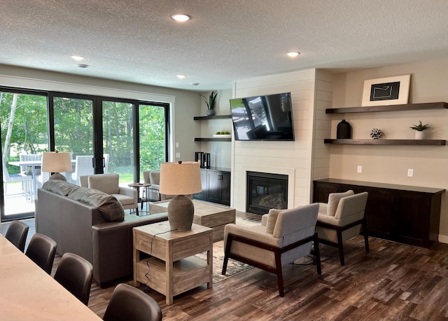 living room with dark hardwood / wood-style floors, a textured ceiling, and a large fireplace