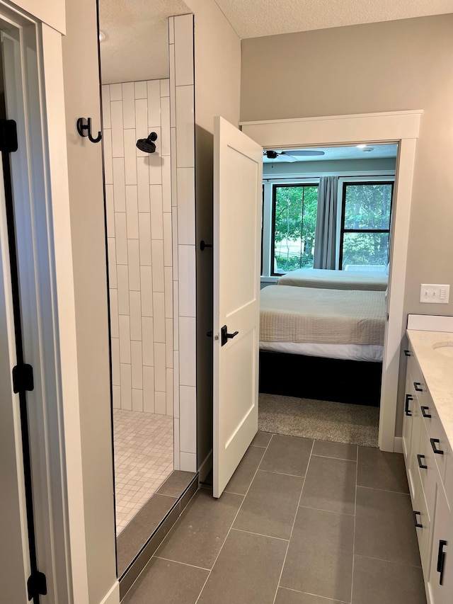 bathroom featuring a textured ceiling, tile flooring, a tile shower, and vanity