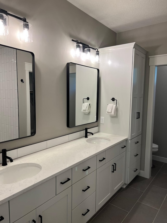 bathroom with a textured ceiling, tile floors, toilet, and dual bowl vanity