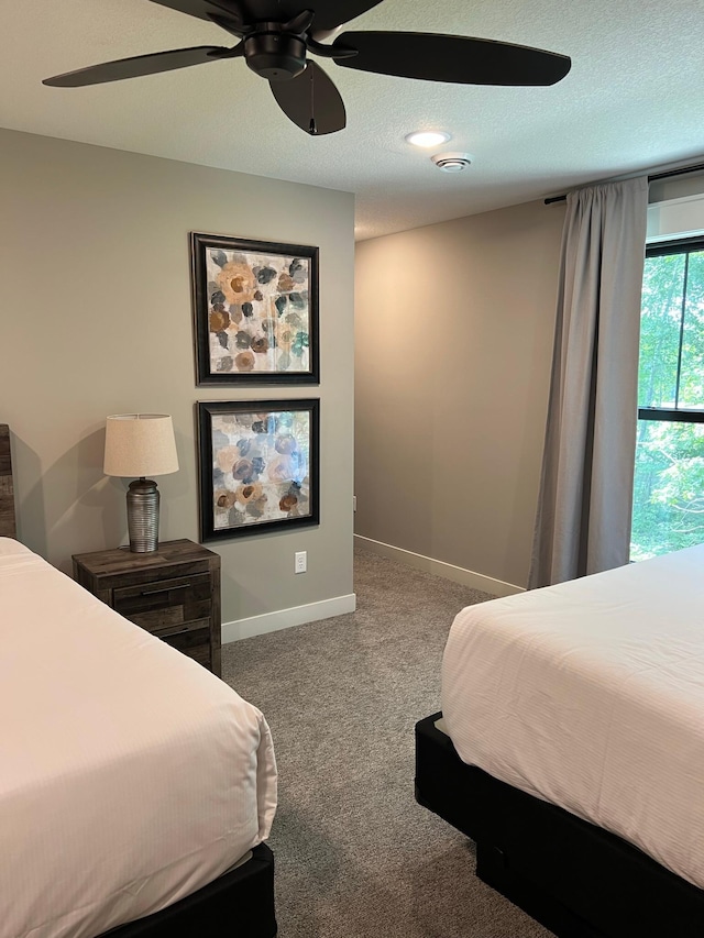 bedroom with a textured ceiling, ceiling fan, and dark carpet