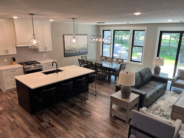 kitchen with pendant lighting, sink, white cabinets, dark wood-type flooring, and stainless steel range with gas stovetop