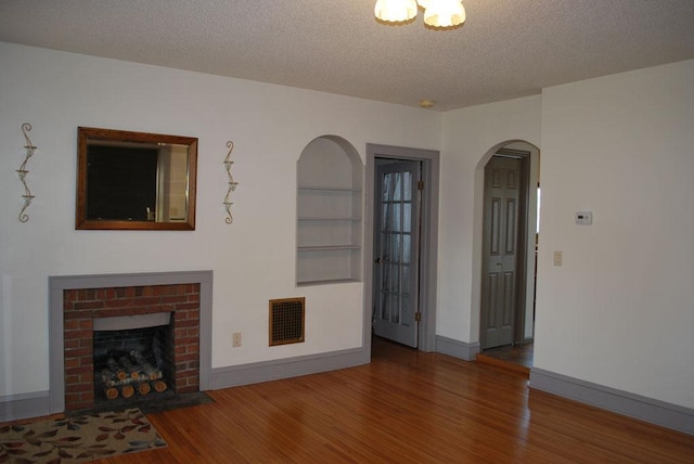 unfurnished living room featuring a textured ceiling, dark hardwood / wood-style floors, built in shelves, and a brick fireplace