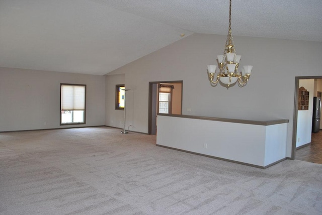 carpeted spare room featuring a notable chandelier, a textured ceiling, and high vaulted ceiling