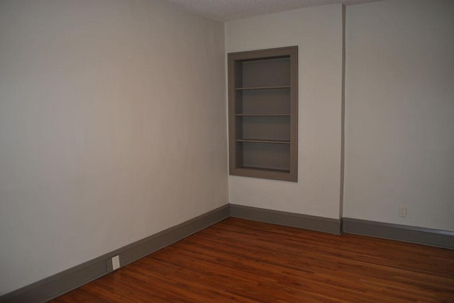 spare room with built in features and dark hardwood / wood-style flooring