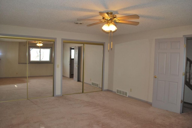 unfurnished bedroom featuring multiple closets, ceiling fan, a textured ceiling, and light carpet