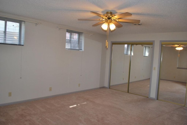 unfurnished bedroom with light carpet, two closets, a textured ceiling, and ceiling fan