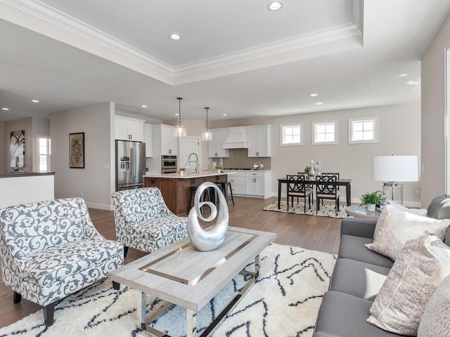 living room featuring a tray ceiling, sink, and light hardwood / wood-style flooring