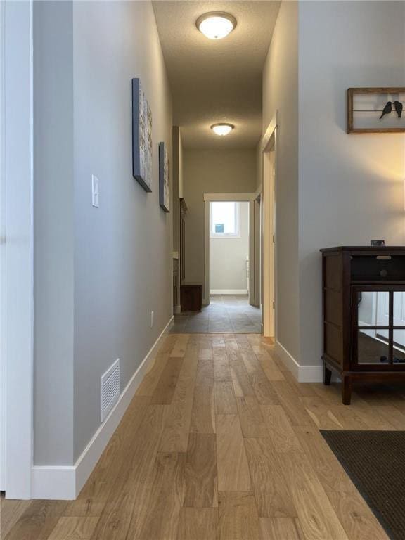 hall featuring baseboards, visible vents, and light wood-style floors