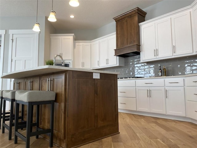 kitchen featuring a breakfast bar, decorative light fixtures, decorative backsplash, white cabinets, and an island with sink