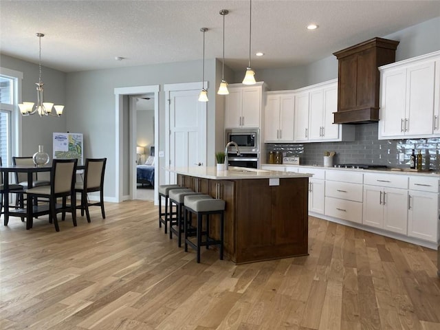 kitchen featuring light countertops, a kitchen island with sink, decorative light fixtures, and white cabinetry